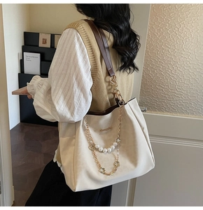 Detail view of large beige tote bag with pearl chain and brown leather shoulder strap