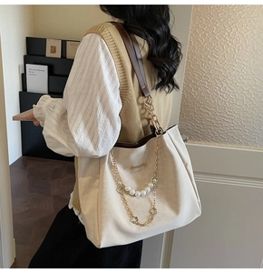 Detail of beige tote bag showing pearl chain strap and brown leather trim on a model