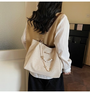 Detail of cream tote bag with pearl chain, floral charm and textured leather finish
