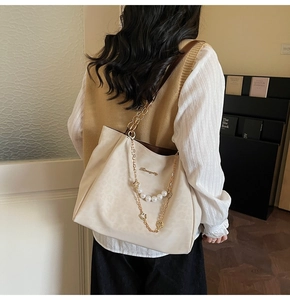 Detail of beige leopard embossed tote bag with gold chain and pearl charm accessory