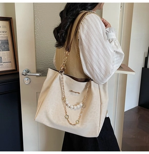 Detail of a large beige tote bag with a gold pearl chain strap and brown leather handle