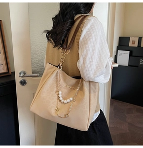 Detail of beige tote bag with gold logo, pearl chain, and clover metal charms on strap