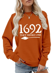 Detail of orange sweatshirt with 1692 They Missed One print and white broom graphic