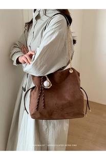 Detail of brown suede tote bag with golden chain strap and baseball pendant charm