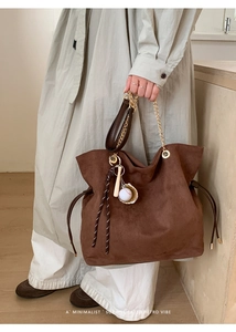 Close-up of brown suede bucket bag with gold chain strap and baseball charm detail