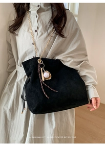 Detail of black suede drawstring bucket bag with gold chain and baseball charm on model