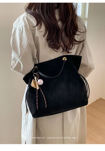 Detail of black suede tote bag with golden hardware and baseball charm accessory