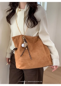 Brown suede tote bag with chain strap and baseball charm detail on white knit top