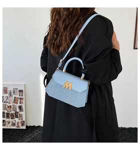 Nahaufnahme der hellblauen Handtasche mit Fischgrätenmuster und goldener M-förmiger Schnalle