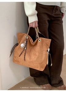 Close-up of retro brown suede tote bag featuring gold chain handles and baseball charm