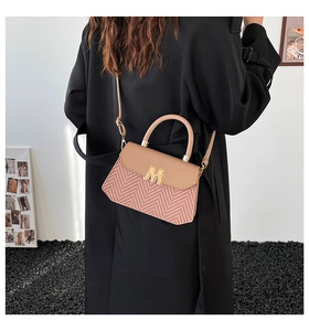 Detail of contrast stitching handbag with woven texture and gold M logo on a model