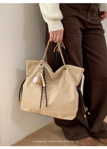 Close-up of a beige suede tote bag with a golden chain handle and a baseball keychain charm