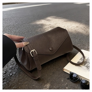 Detail of dark brown crossbody bag with flap cover and adjustable strap on asphalt