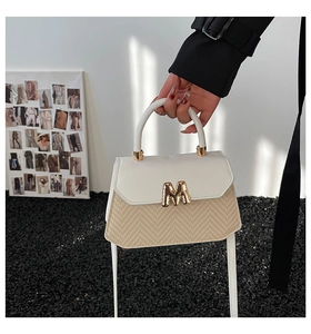 Detail of a minimalist two-tone handbag featuring a textured fabric base and golden M hardware