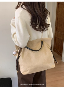 Detail of minimalist beige suede tote bag featuring black handle and gold chain strap