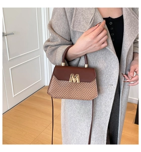 Detail of a brown two-tone straw tote bag featuring a metallic M logo and leather flap