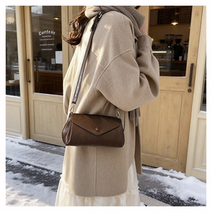 Brown vintage leather envelope crossbody bag styled with a beige coat in winter