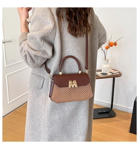 Detail van een crossbodytas met geweven textuur, lederen bies en gouden M-sluiting
