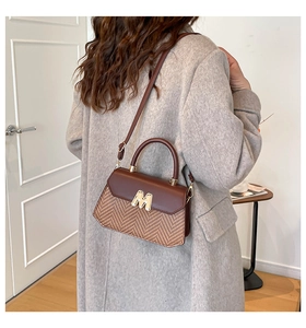 Detail einer braunen Patchwork-Handtasche mit Webstruktur und goldener M-Metall-Hardware