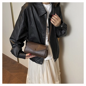 Detail of dark brown leather accordion crossbody bag with litchi texture and round buckle