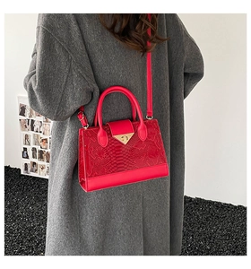 Dettaglio borsa in pelle rossa strutturata con chiusura dorata su un cappotto grigio