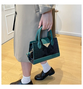 Detail of green faux snakeskin leather handbag with triangular metal clasp on coat