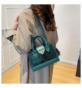 Borsa a mano verde effetto serpente con chiusura dorata indossata a spalla da una modella