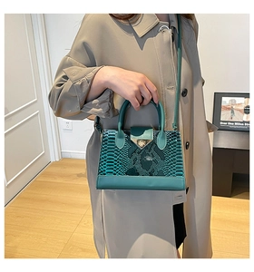 Close-up of a peacock green crocodile pattern handbag with gold clasp on a beige coat