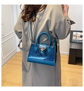 Close-up of blue faux-crocodile leather handbag with gold metal lock and shoulder strap