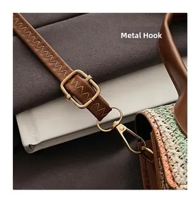 Detail of the golden hardware lobster clasp and adjustable brown leather strap on a woven bag