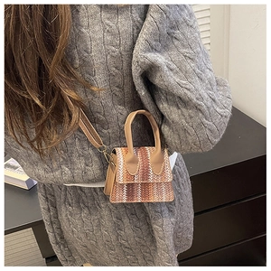 Detail of woven square handbag with brown leather handle on casual sweater