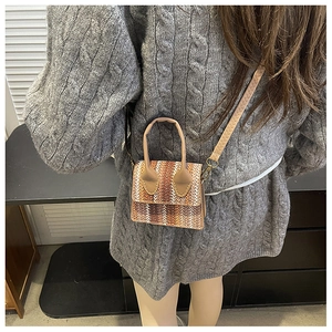 Detail of a brown woven mini crossbody bag showing texture on a grey knitted sweater