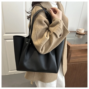 Woman in camel coat carrying a large black matte leather tote bag with metal studs