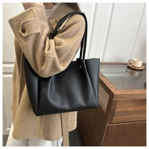 Close-up of a black leather tote bag with silver studs worn with a camel wool coat
