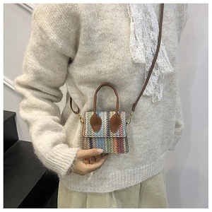 Detail of colorful woven straw bag with blue, orange, and beige stripes and brown handles