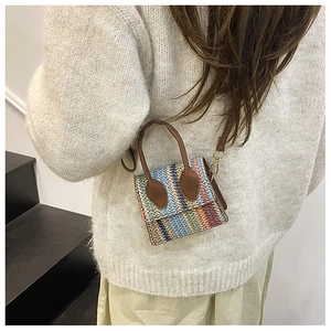 Model wearing a mini multi-color woven crossbody bag with brown leather handle strap