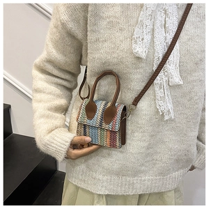 Detail of colorful woven straw mini bag with brown leather handles and striped texture