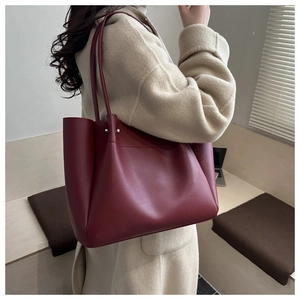Side view of a burgundy tote bag in matte leather worn with a beige wool coat
