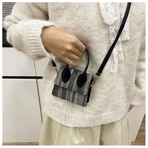 Detailed close-up of mini woven tweed handbag with black leather handle and gold hardware