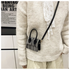 Close-up of a mini crossbody bag featuring a classic woven pattern and black leather handles
