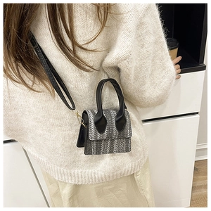 Detail of mini woven crossbody bag on shoulder, showing texture and compact size