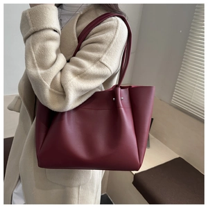 Burgundy oversized leather tote bag with silver studs worn by a model in a minimalist setting