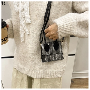 Detail of woven texture mini crossbody bag with black handle and gold metal hardware