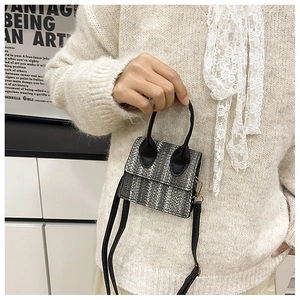 Detailed view of mini woven straw bag with black handles and gold hardware on beige sweater