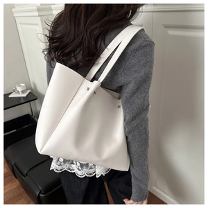 Modern white soft leather tote bag shown on shoulder in a minimalist urban setting