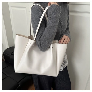Minimalist beige tote bag with silver studs and smooth leather texture shown on shoulder