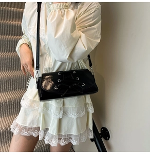 Close-up of black lace-up shoulder bag with bow detail on white lace dress