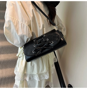 Detail of black glossy shoulder bag featuring corset-style lace-up design with metal eyelets