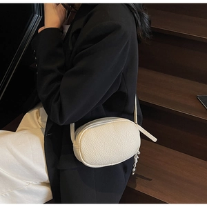 Close-up of white lychee texture crossbody bag worn by model over a black blazer suit