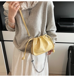 Close-up of glossy yellow drawstring bucket bag with silver chain and leather strap